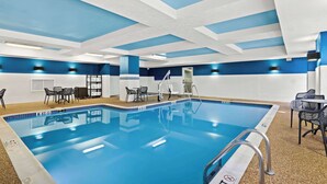 A swimming pool with clear blue water, surrounded by lounge chairs and a tiled deck.