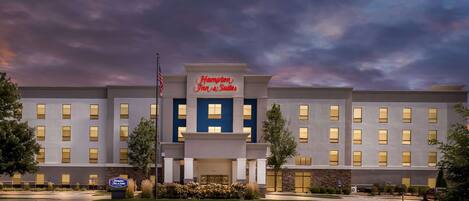 Un hotel Hampton Inn & Suites con una fachada moderna, numerosas ventanas y un césped delantero bien cuidado.