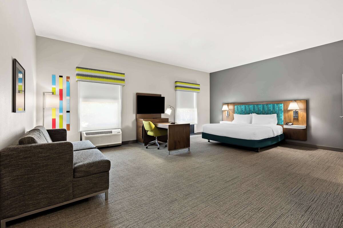 A hotel room with a bed, a desk, a chair, and a sofa.