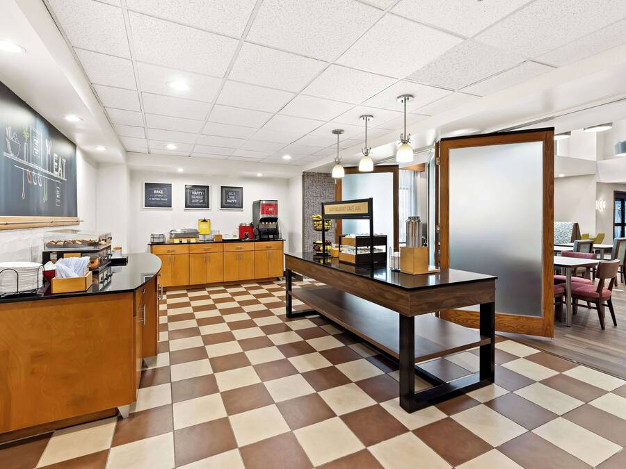 Um café moderno com piso xadrez, balcão de madeira e cardápio em lousa.