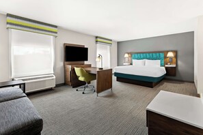A hotel room with a bed, a desk with a chair, a TV, and a large window.