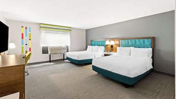 A hotel room with two beds, a desk, a chair, a TV, and a window with blinds.