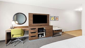 Habitación de hotel con un escritorio de madera, una silla verde, televisor de pantalla plana, microondas, un estante pequeño y una cama.