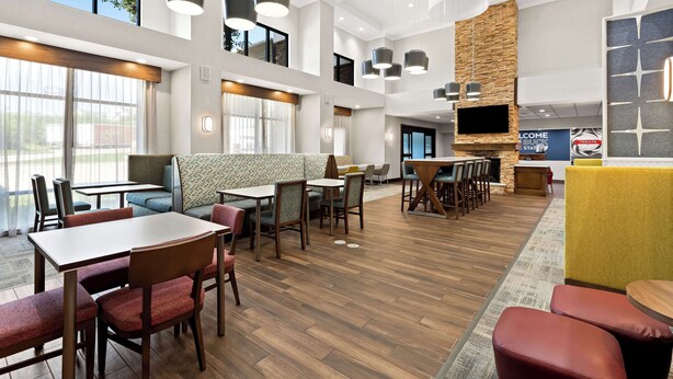 A spacious hotel lobby with multiple seating areas, including tables and chairs, and a large TV screen.