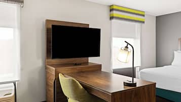 Ein Hotelzimmer mit einem Holztisch, einem Fernseher, einem grünen Sessel, einer Lampe und einem Bett.