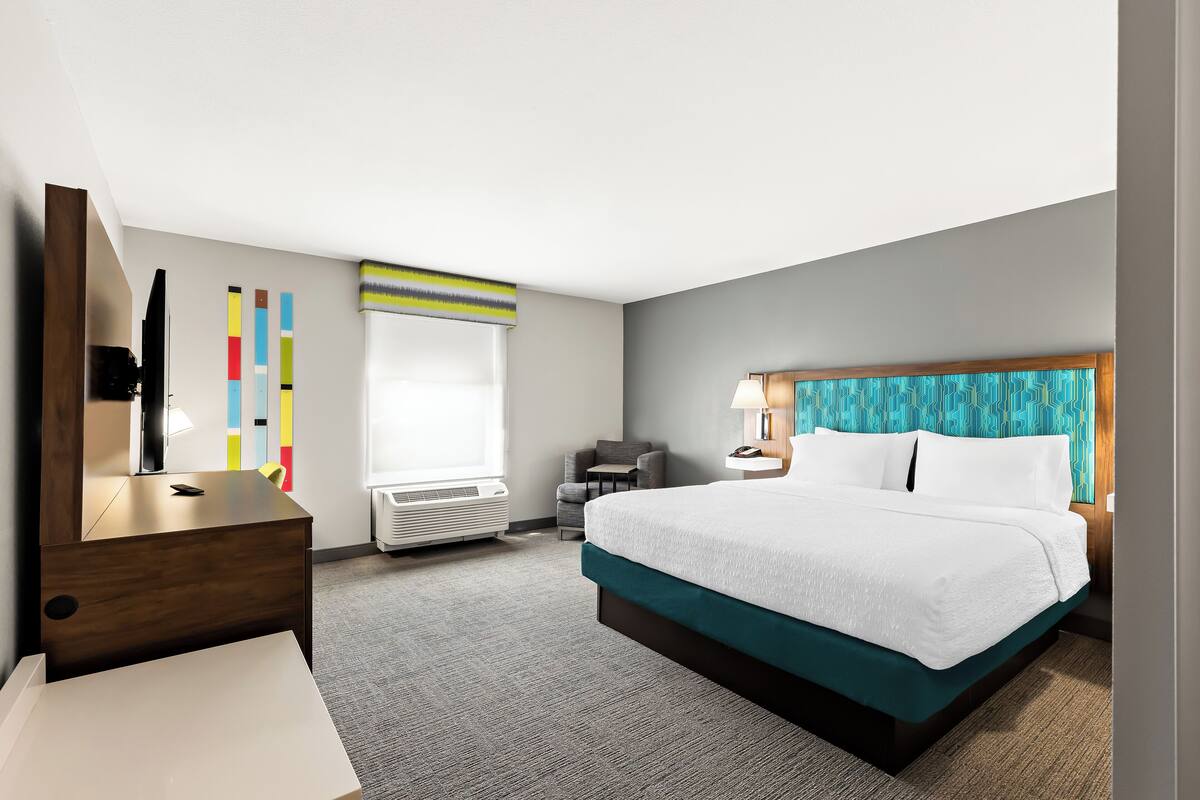 A hotel room with a bed, a desk, a chair, a TV, and a window.