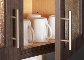 Un mueble de madera con un tirador metálico, que contiene varias tazas de cerámica blanca.