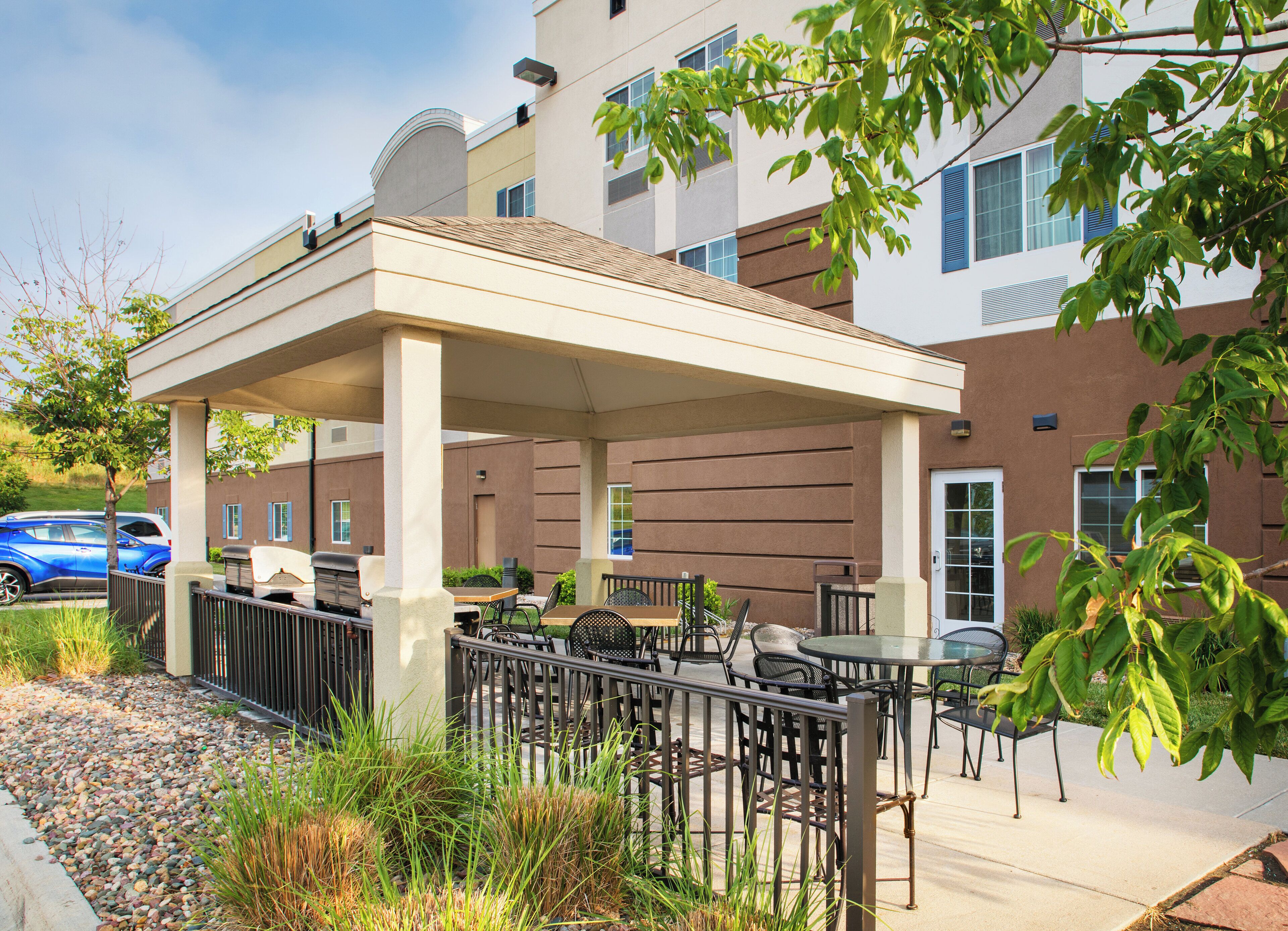 An outdoor patio area with tables and chairs, a covered seating area, and a building in the background.