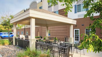 An outdoor patio area with tables and chairs, a covered seating area, and a building in the background.