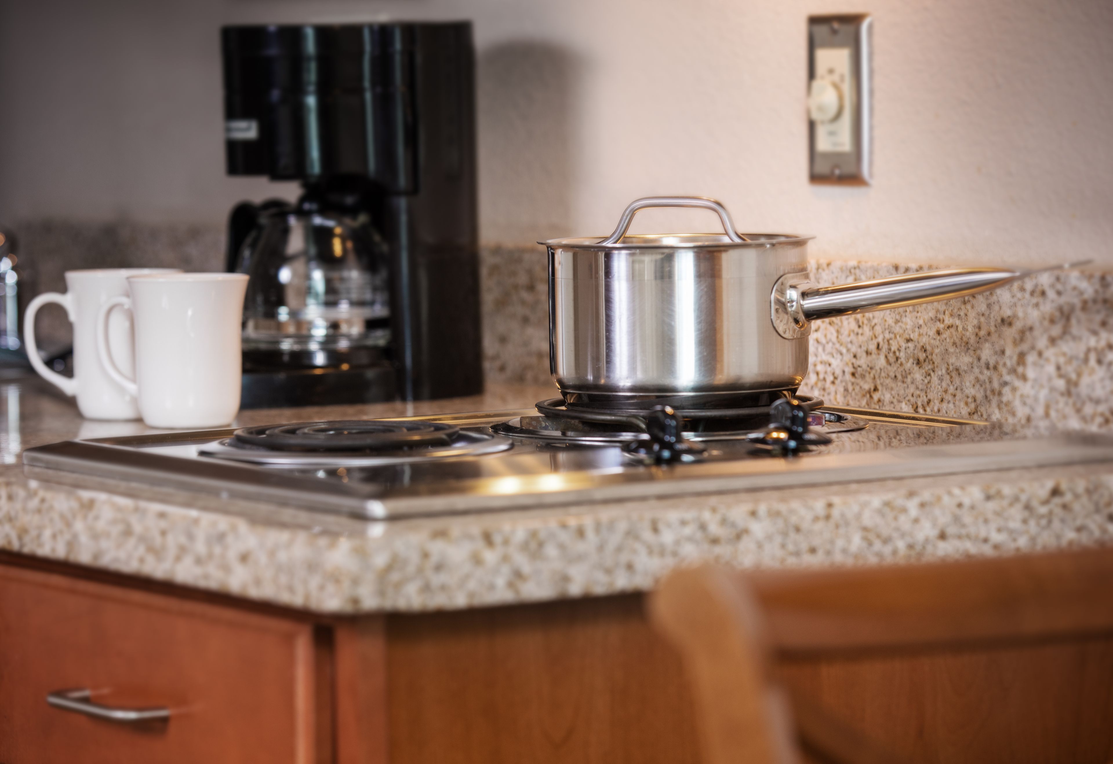 Une cuisine équipée d’une cuisinière, d’une machine à café et d’une casserole posée sur le plan de travail.