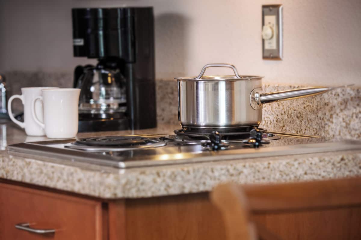 A kitchen with a stove, a coffee maker, and a pot on the counter.