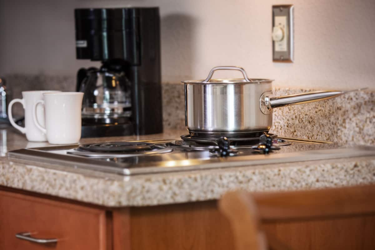 A kitchen with a stove, a coffee maker, and a pot on the counter.