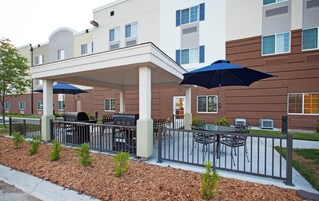 An outdoor patio area with tables and chairs, covered by umbrellas, and a barbecue grill.