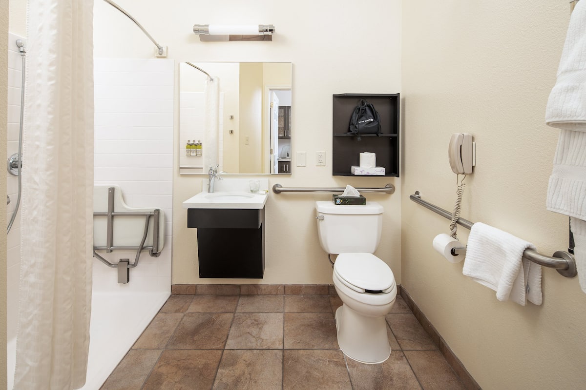 A bathroom with a toilet, sink, and shower. There is a towel rack and a phone on the wall.
