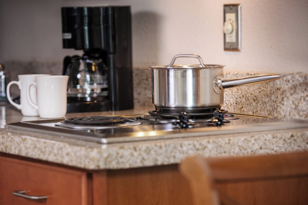 Una cocina con estufa, cafetera y una olla sobre la encimera.
