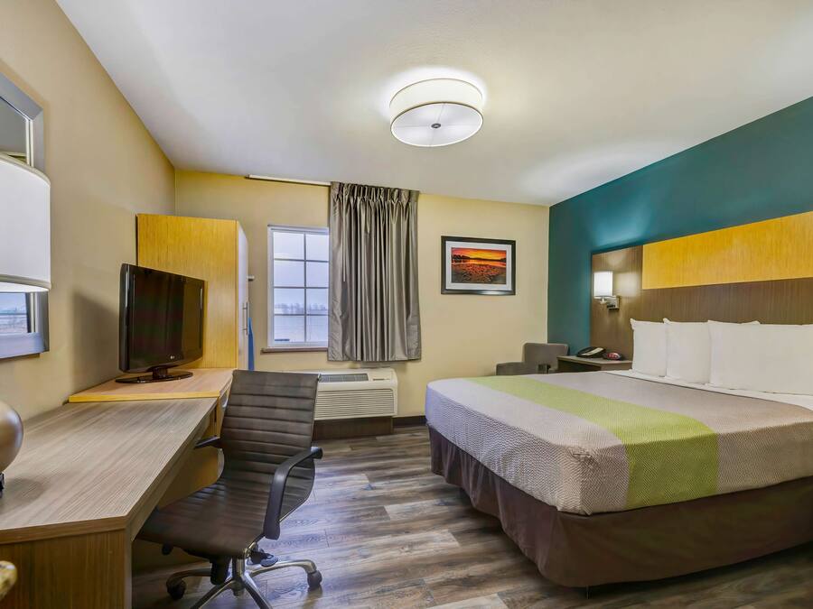 A hotel room with a bed, desk, chair, TV, and a window with curtains.