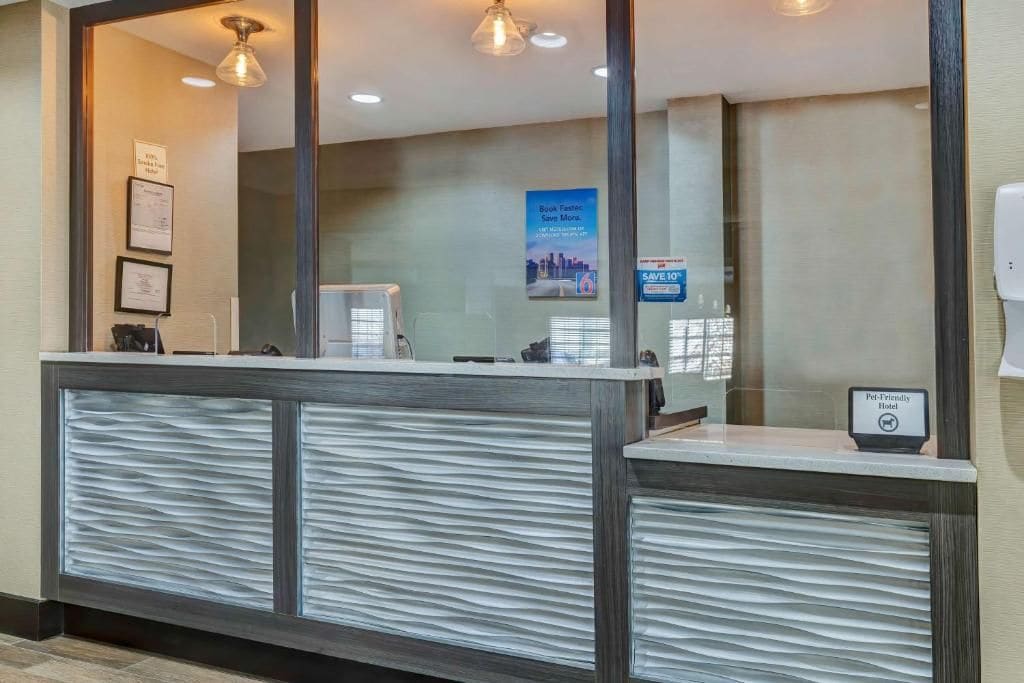 Een receptiebalie met een glazen scheiding, ingelijste certificaten en een bordje 'Huisdiervriendelijk Hotel'.