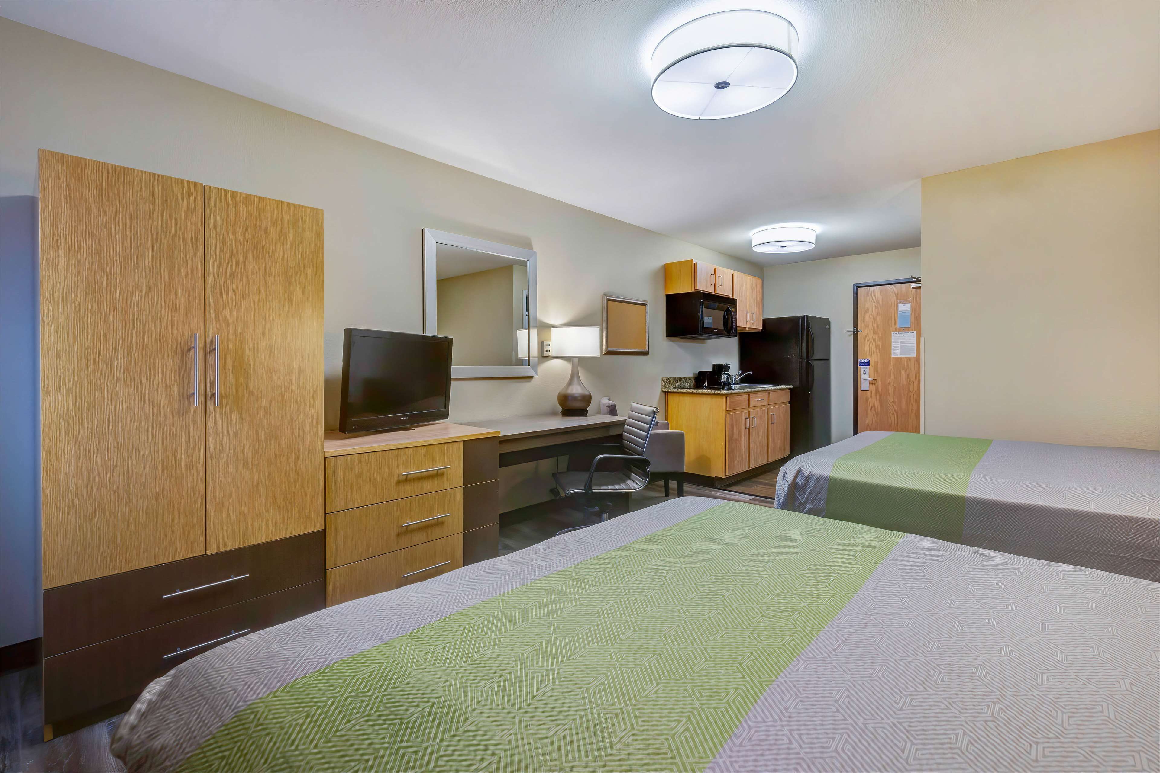 A hotel room with a bed, a desk with a computer, a TV, a microwave, and a refrigerator.