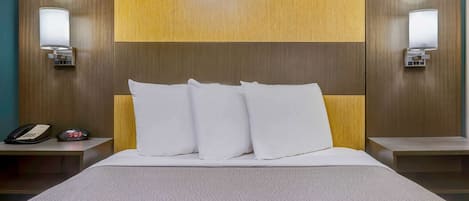 A hotel room with a wooden headboard, two bedside tables, a bed with white bedding, and a nightstand with a phone and alarm clock.