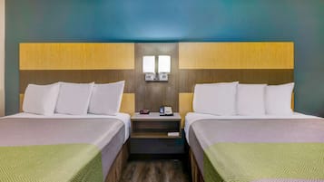 Habitación de hotel con dos camas, una mesita de noche con teléfono y reloj, y una lámpara de pared.