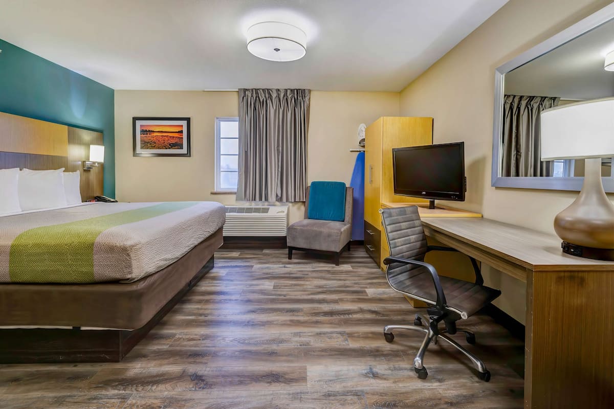 A hotel room with a bed, desk, chair, television, and a large mirror.