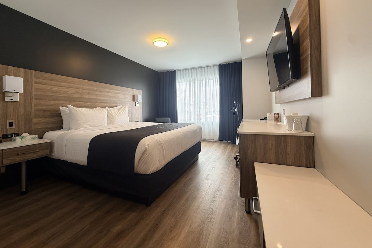 Une chambre d’hôtel moderne dotée d’un grand lit, d’une tête de lit en bois, d’un téléviseur à écran plat, d’un bureau avec une chaise et d’un espace salle de bain.