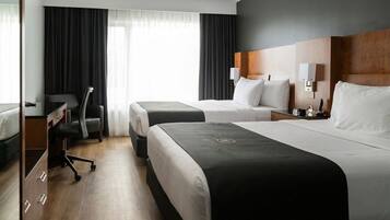 A hotel room with two beds, a desk, a chair, and a wardrobe.