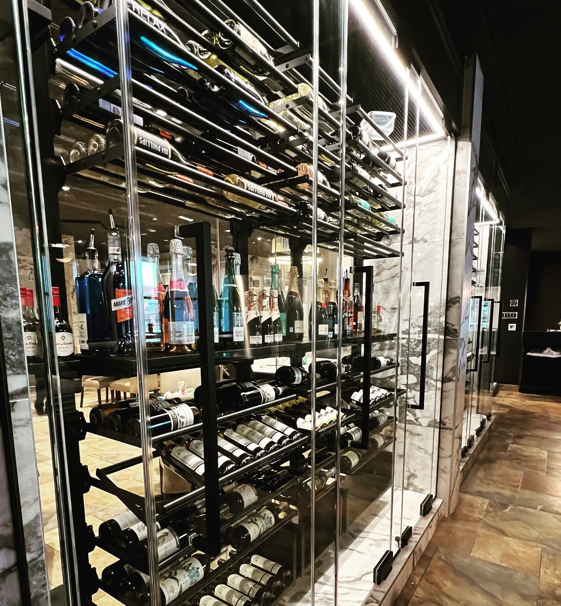 Una bodega con varias estanterías llenas de botellas de vino, una pared de mármol y suelo de madera.