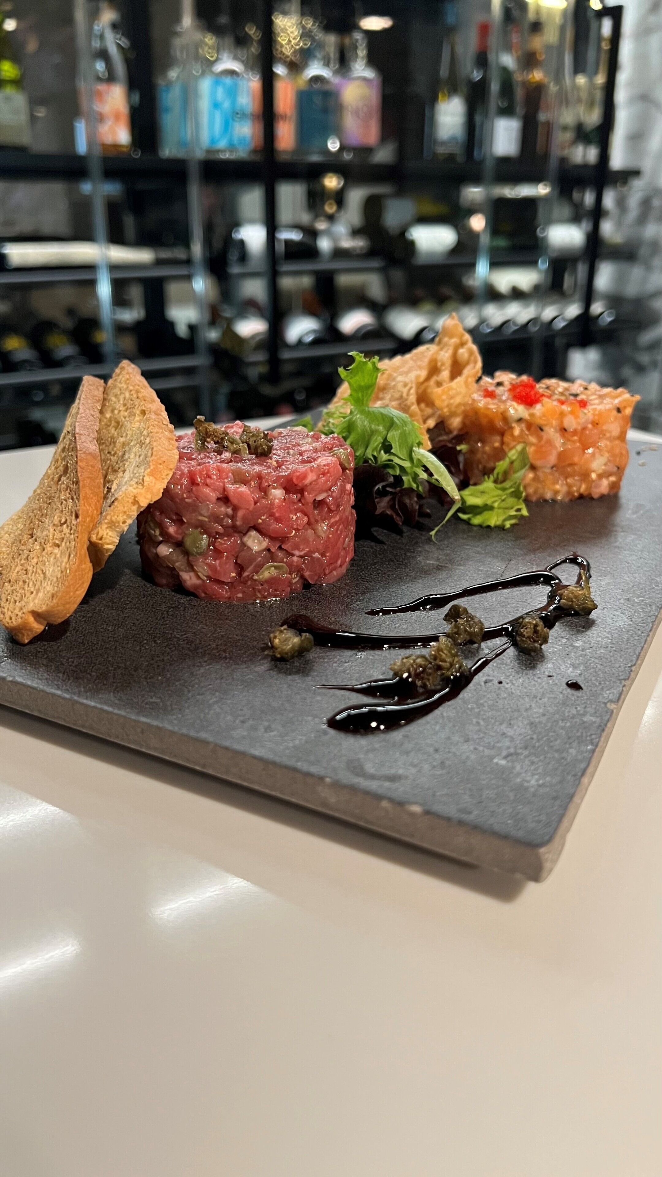 A plate of food with bread and a meat dish, possibly steak tartare, on a slate board.