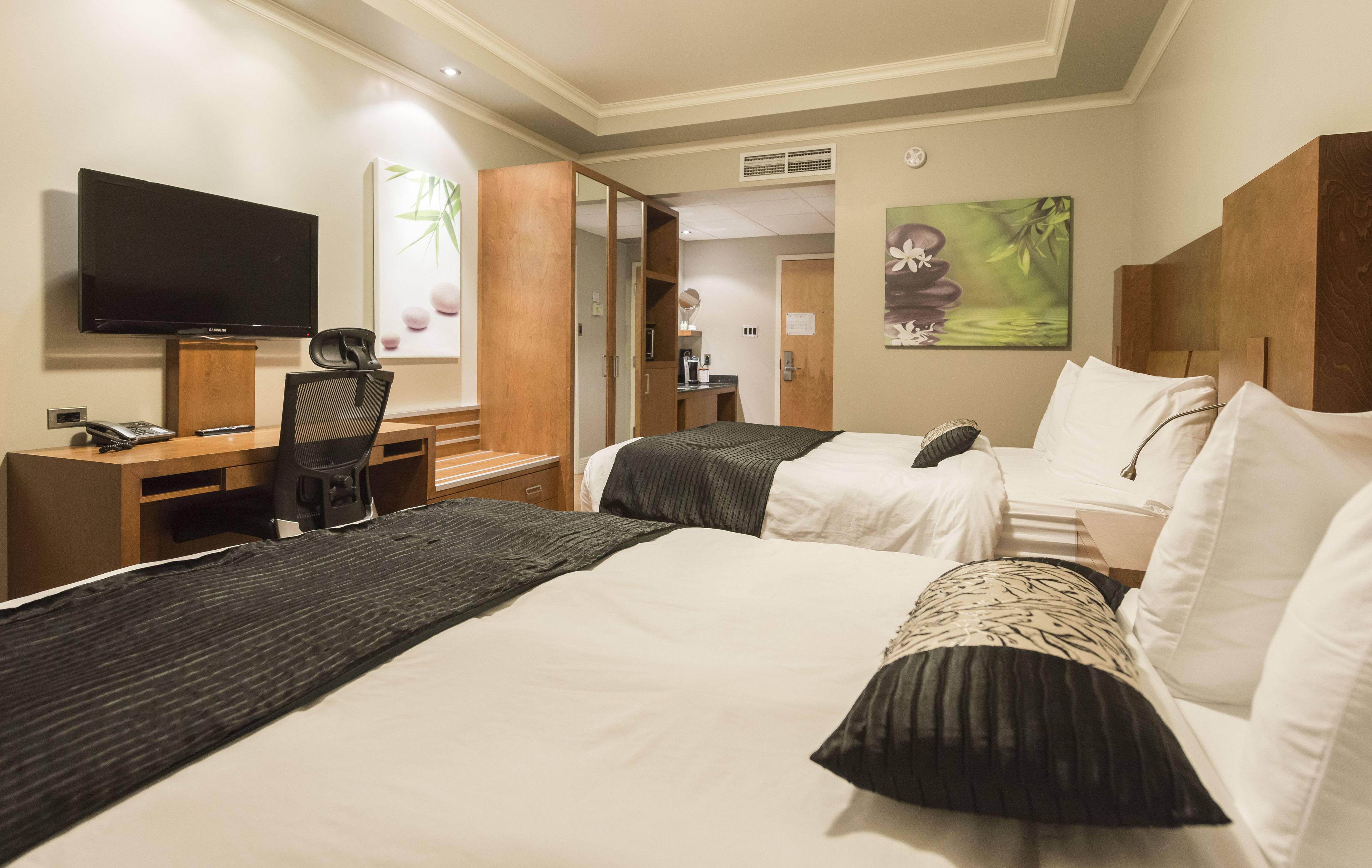 A hotel room with two beds, a desk, a chair, a television, and artwork on the walls.