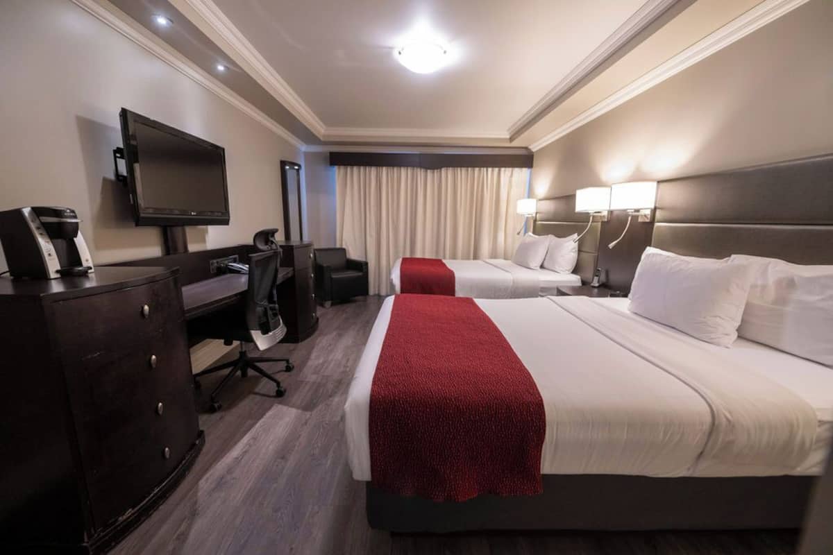 Une chambre d’hôtel avec deux lits, un bureau avec une chaise, une télévision et un mini-bar.