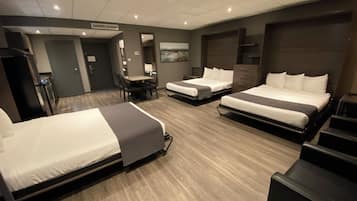 A hotel room with three beds, a desk, and a chair. There is a painting on the wall and a door leading to the bathroom.