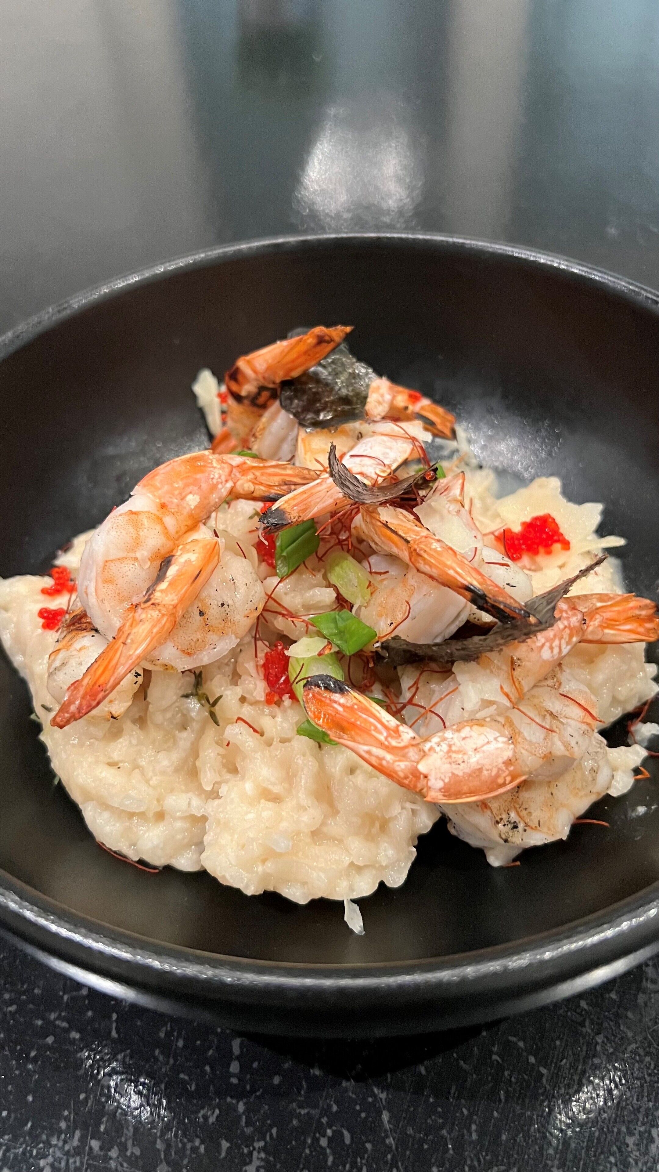 A bowl of seafood risotto with shrimp and garnishes.