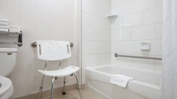 Une salle de bain avec des toilettes blanches, un lavabo blanc muni d’une barre d’appui, une baignoire blanche avec une serviette, et un rideau de douche.