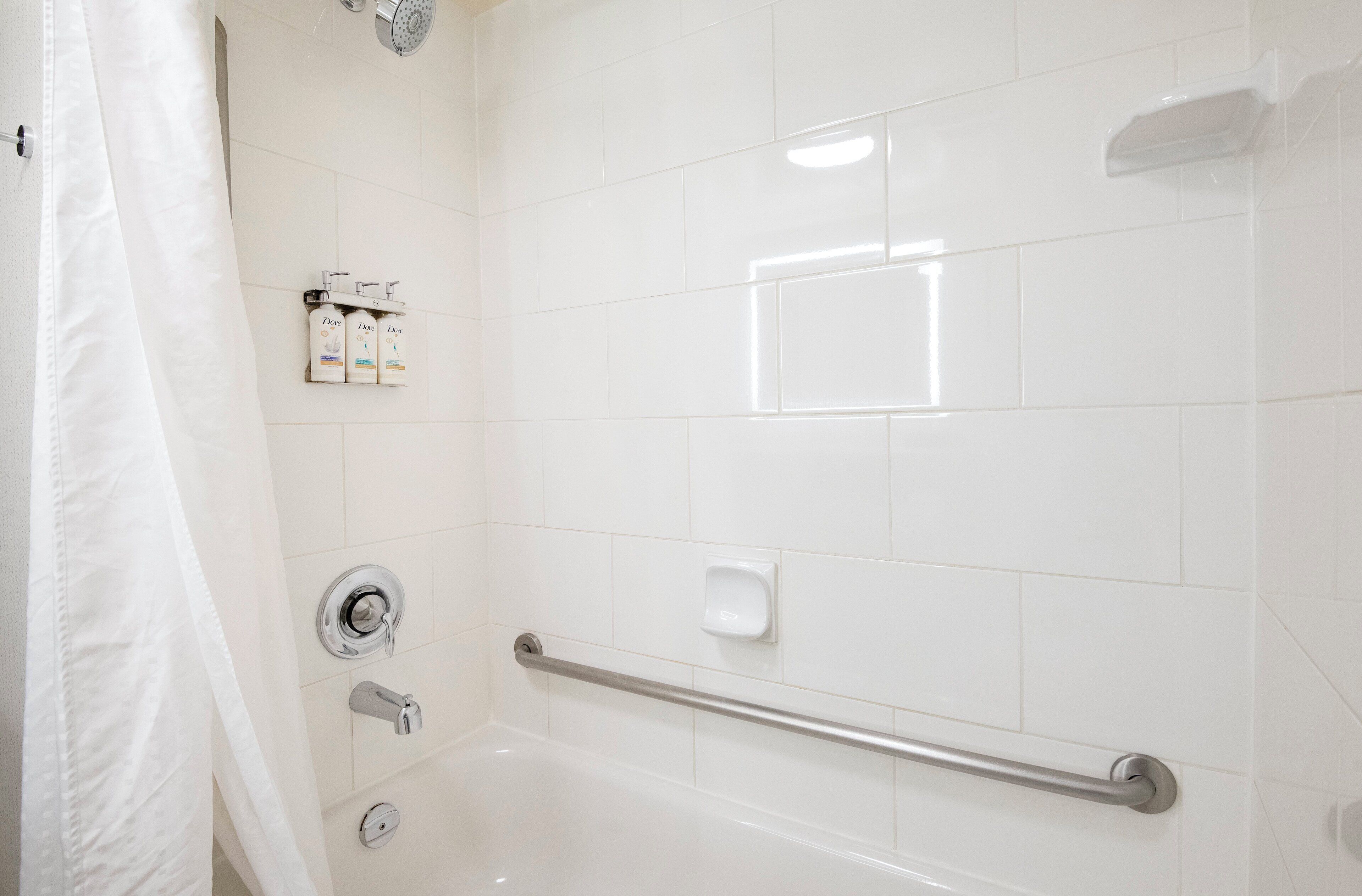 A white bathroom with a bathtub, a handrail, and a showerhead.