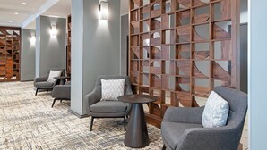 A modern lobby with grey armchairs, a round table, and a wooden decorative wall.