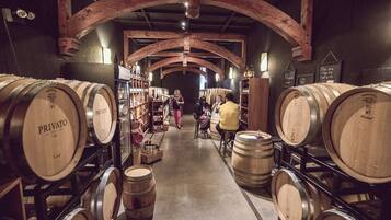 A wine cellar with wooden barrels and shelves of wine bottles.