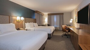 A hotel room with two beds, a desk, a chair, a TV, and a lamp.