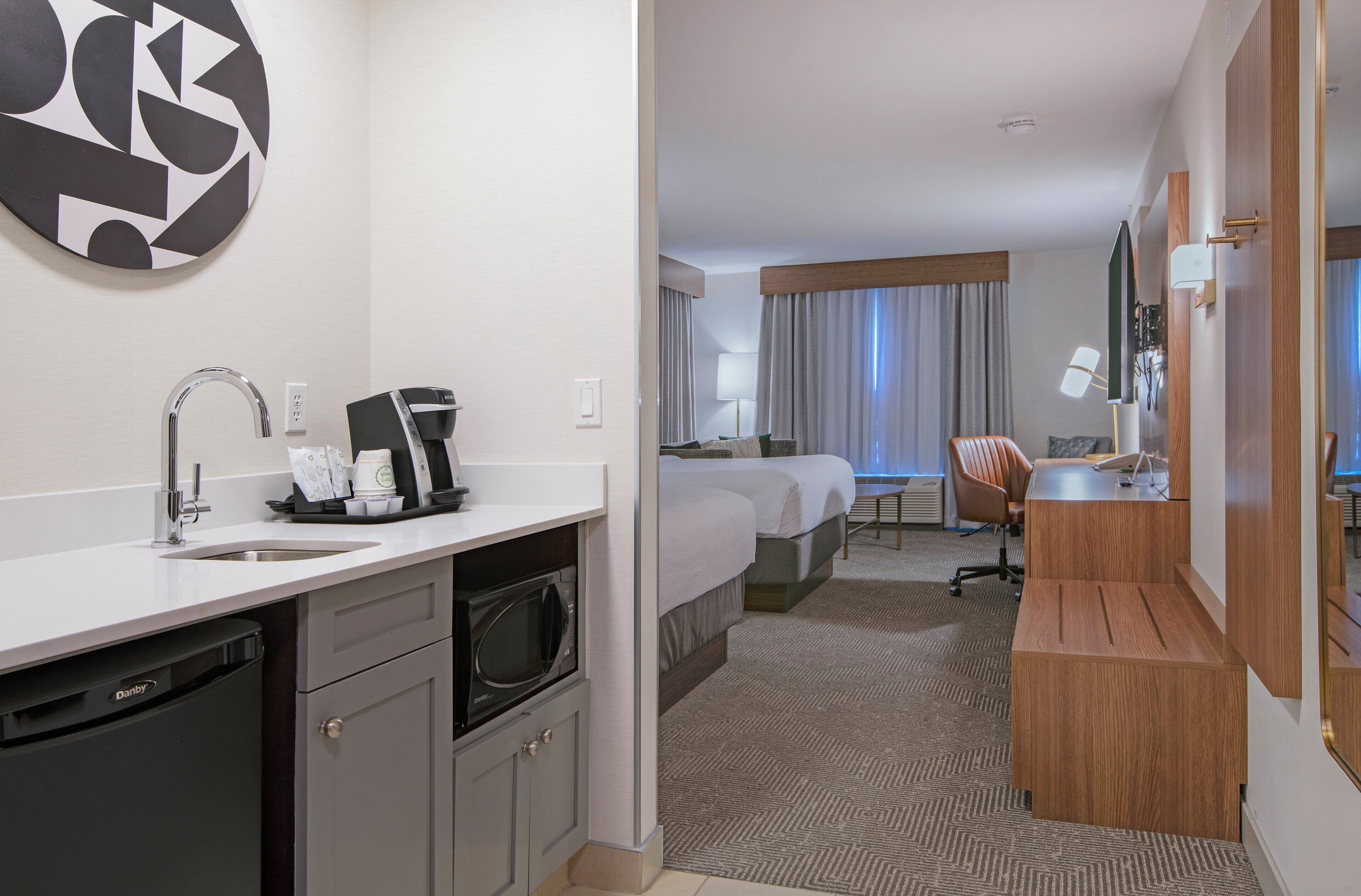 Ett hotellrum med ett litet kök, en säng, ett skrivbord och ett badrum.