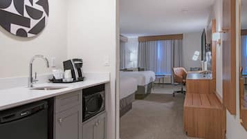 Ett hotellrum med ett litet kök, en säng, ett skrivbord och ett badrum.
