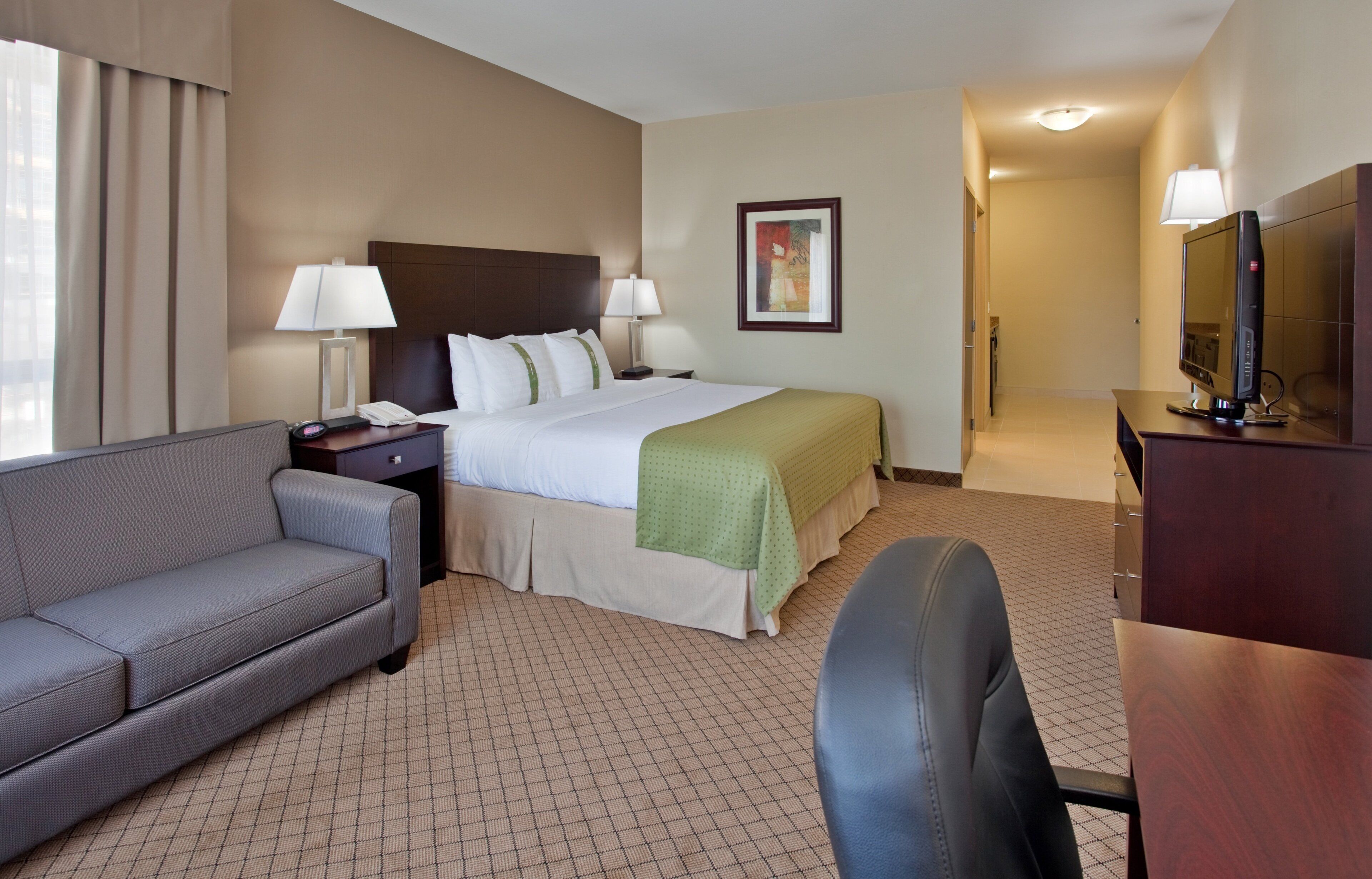 A hotel room with a bed, a desk, a chair, a sofa, and a television.
