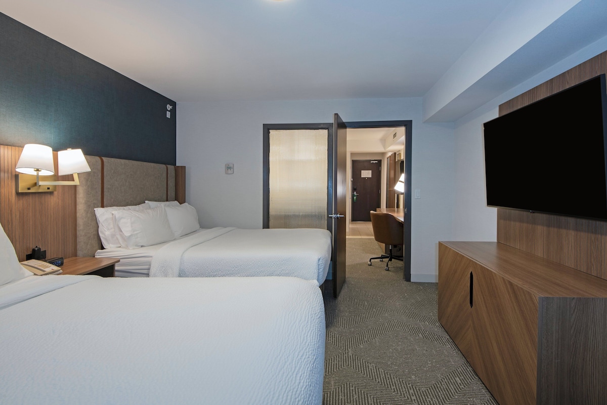 A hotel room with two beds, a TV, a desk, and a bathroom visible through a door.