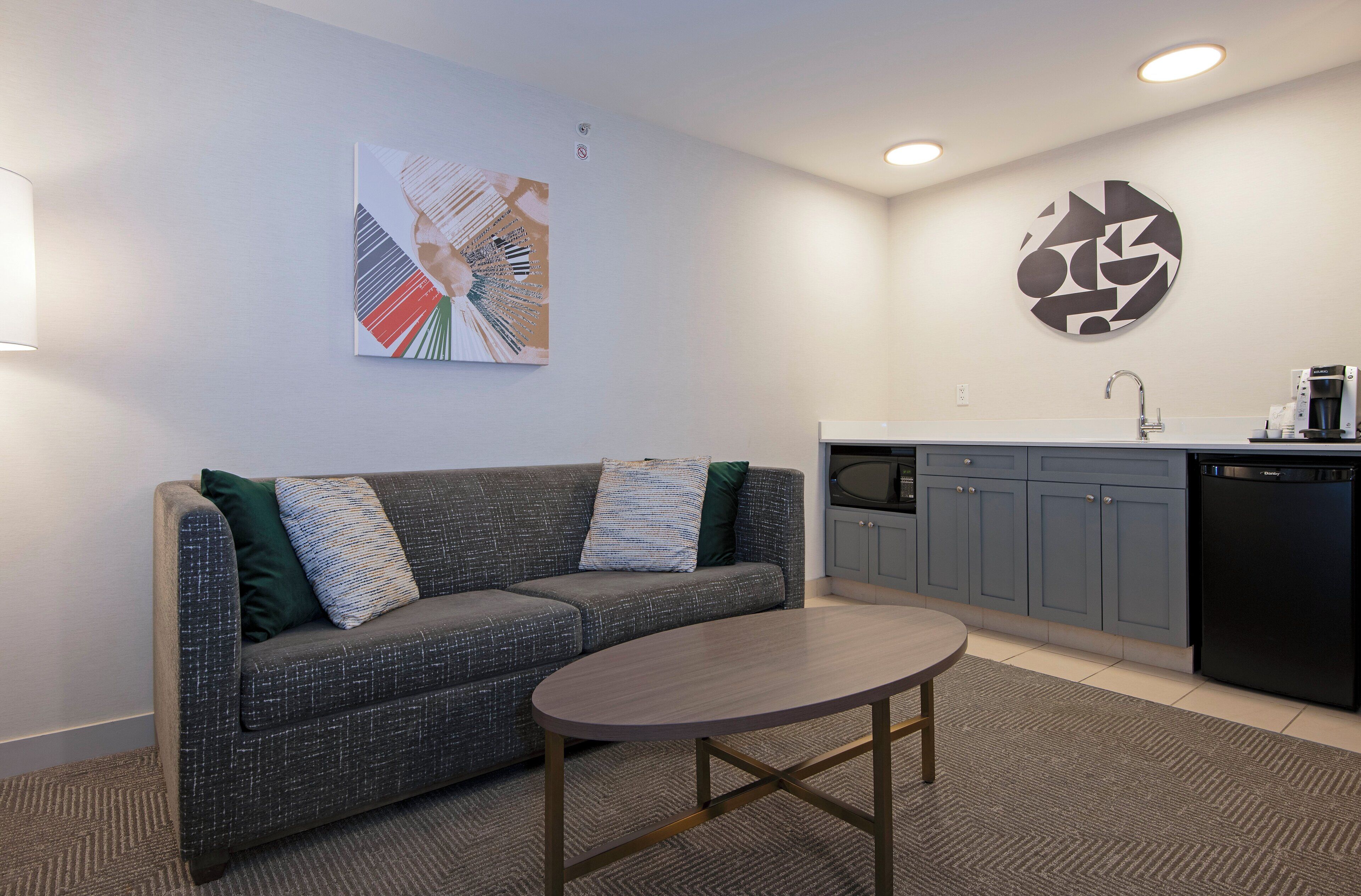 A modern living area with a grey sofa, a round coffee table, and a kitchen with grey cabinets and a black dishwasher.
