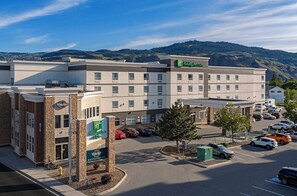 Un hotel Holiday Inn Express con estacionamiento, un restaurante visible y montañas al fondo.