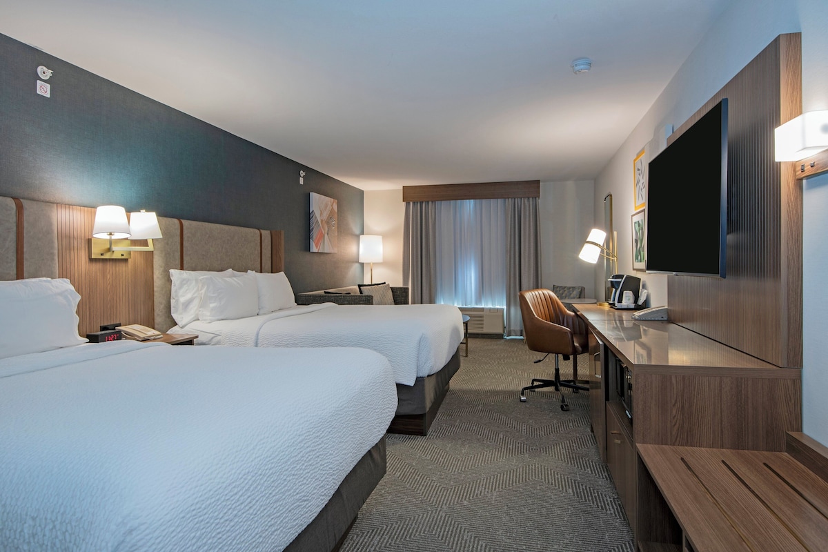 A hotel room with two beds, a desk, a TV, and a chair.