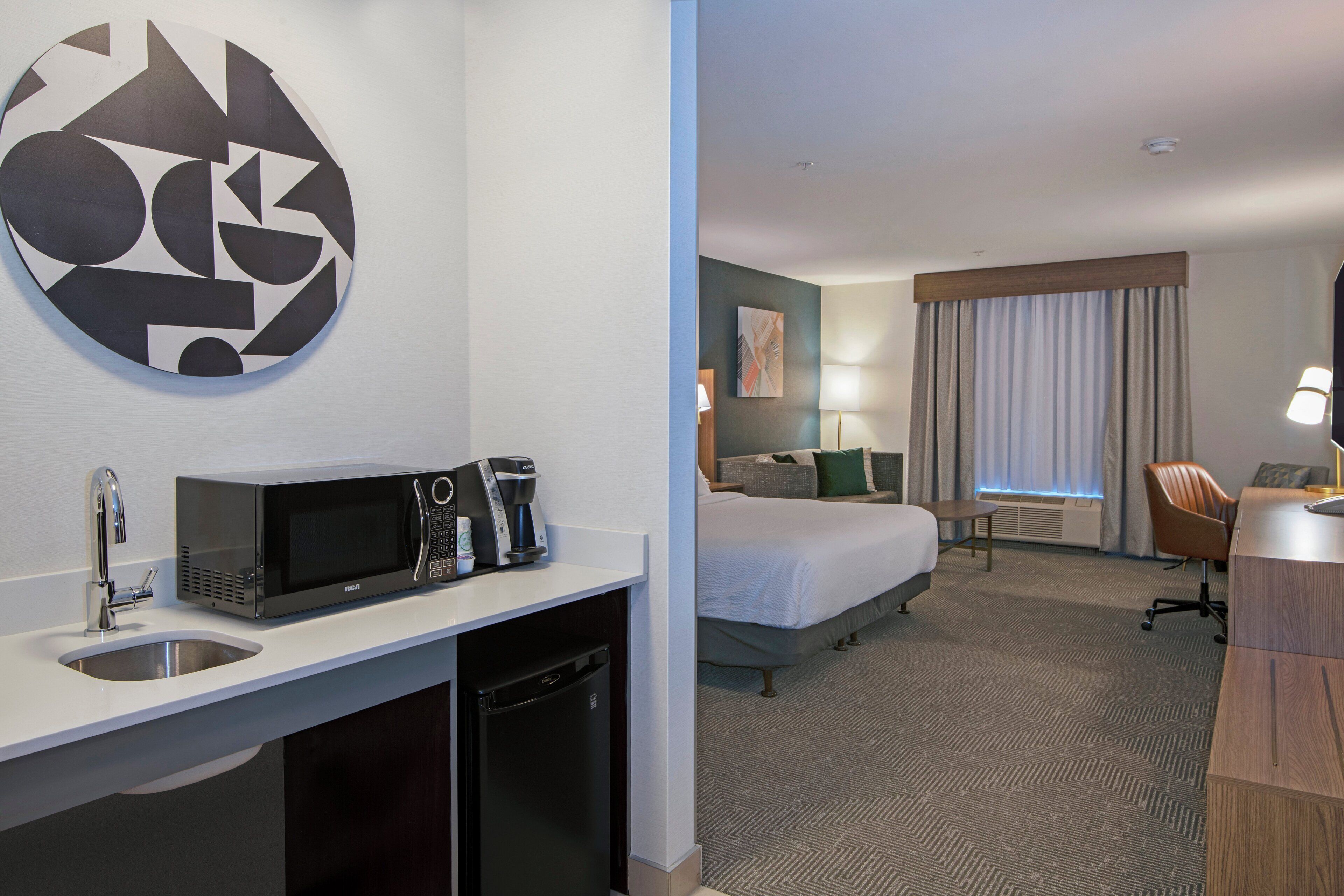 A hotel room with a bed, a desk with a microwave, a coffee maker, and a sink.