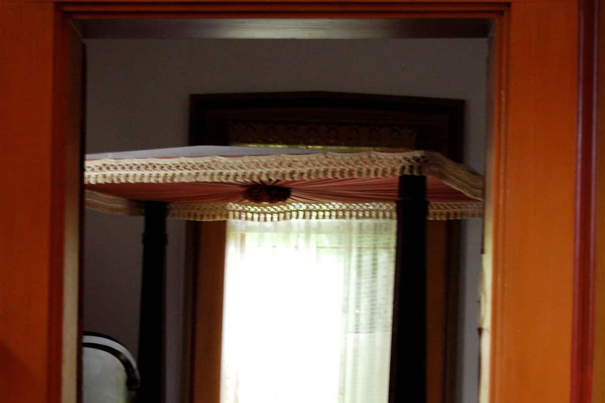 Un pasillo estrecho que conduce a un dormitorio con una cama, una silla y una ventana con cortinas.