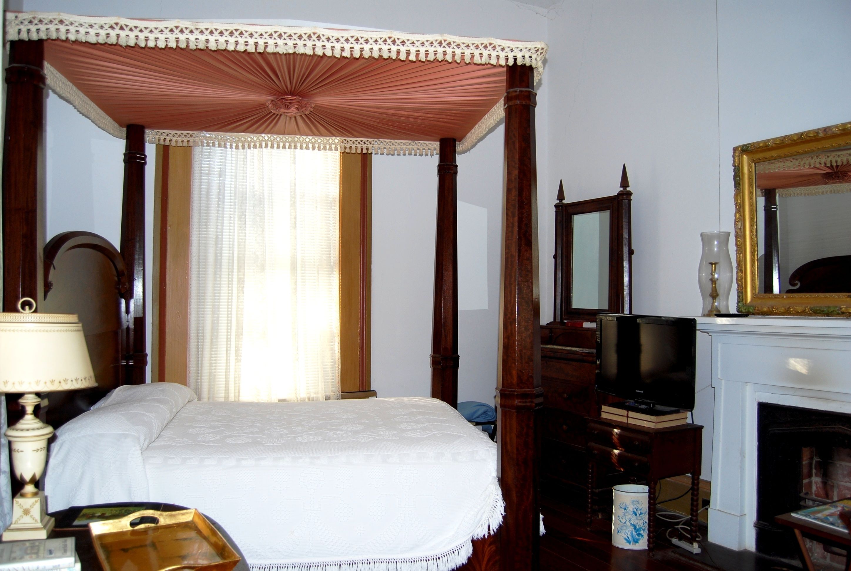 A traditional bedroom with a four-poster bed, a television, and a fireplace.