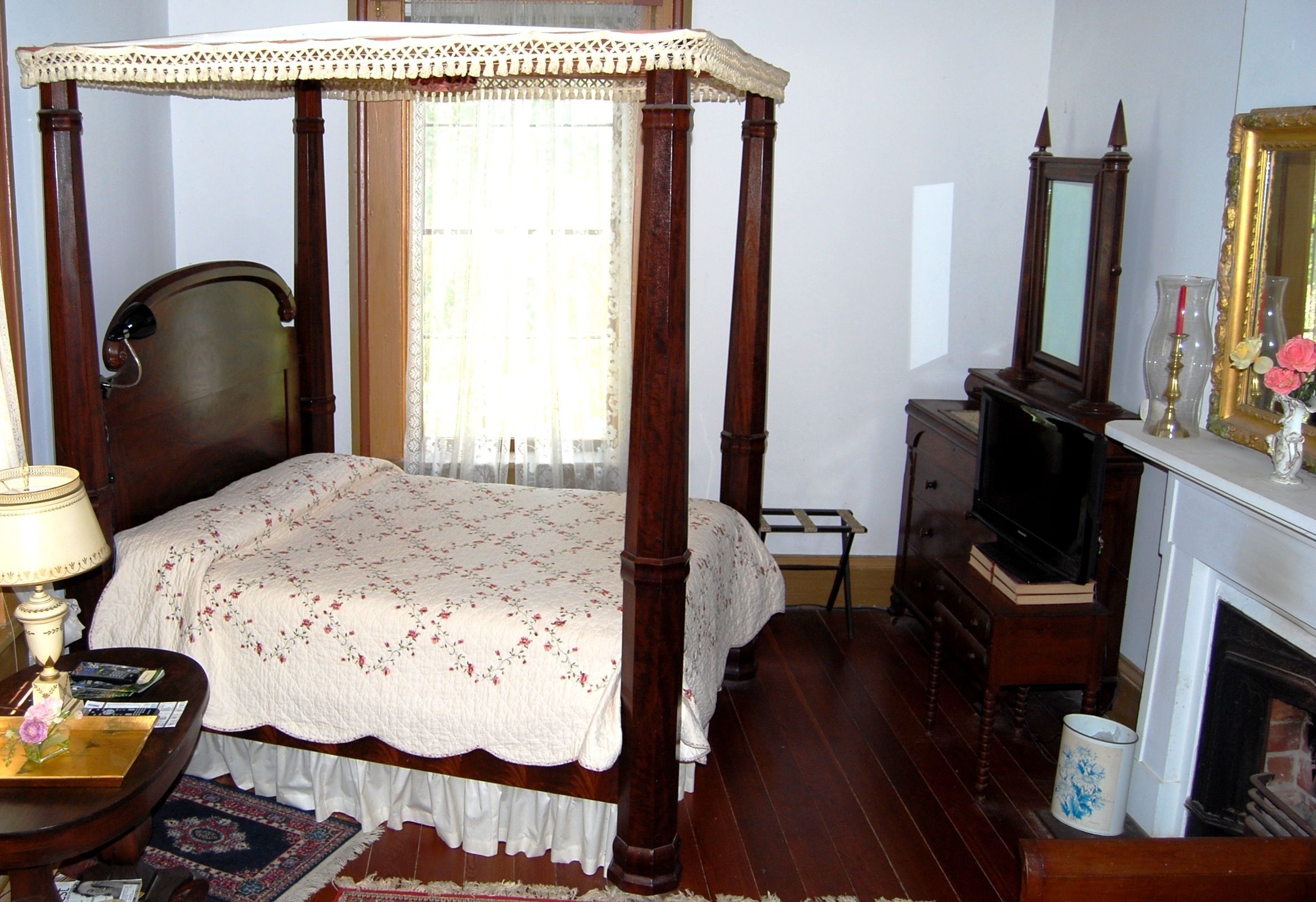 Um quarto tradicional com uma cama de dossel, um penteou de madeira, uma televisão e uma lareira.
