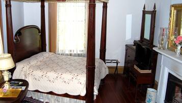 Um quarto tradicional com uma cama de dossel, um penteou de madeira, uma televisão e uma lareira.